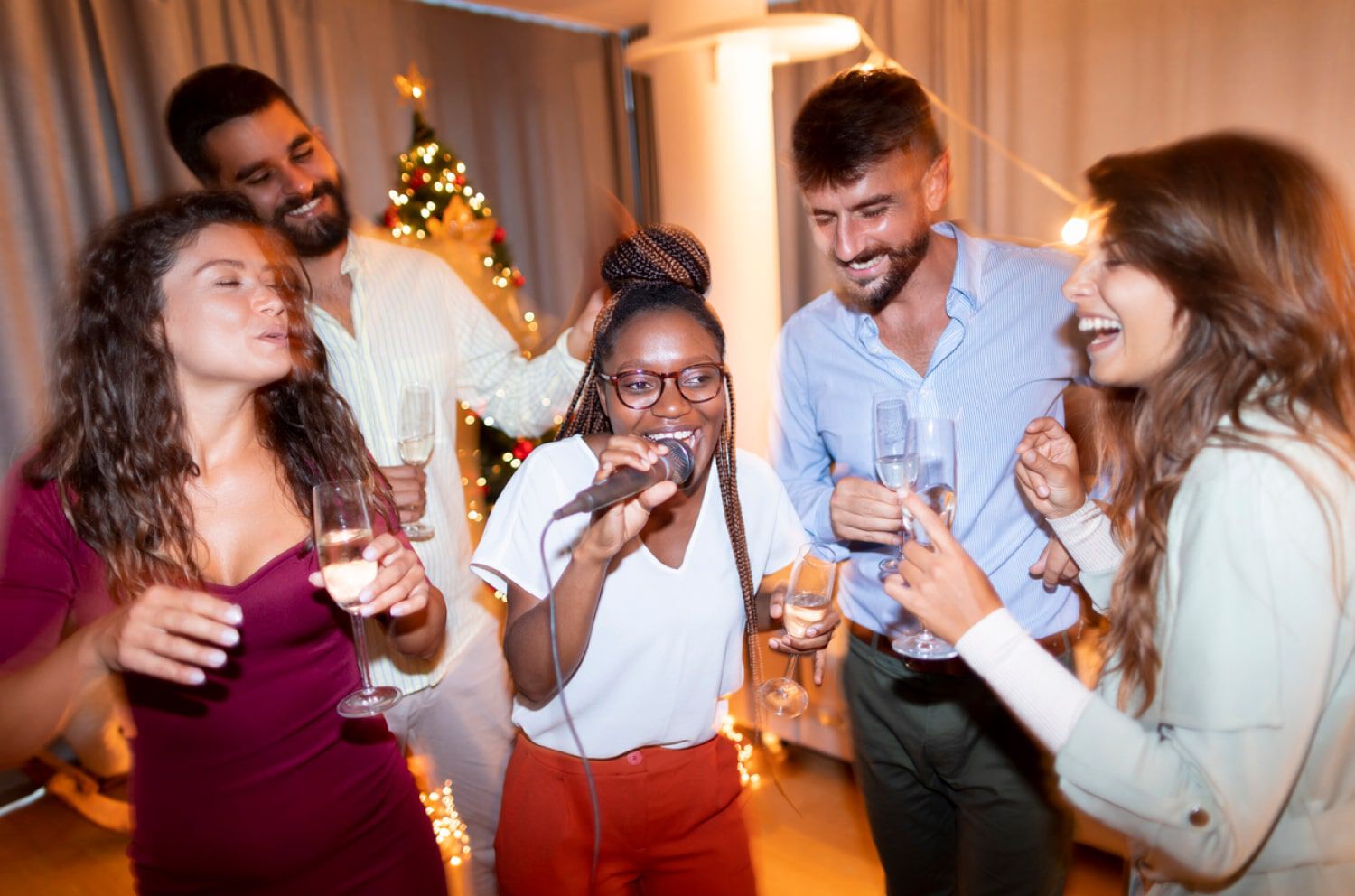 A woman singing into a microphone with friends laughing and singing with her.