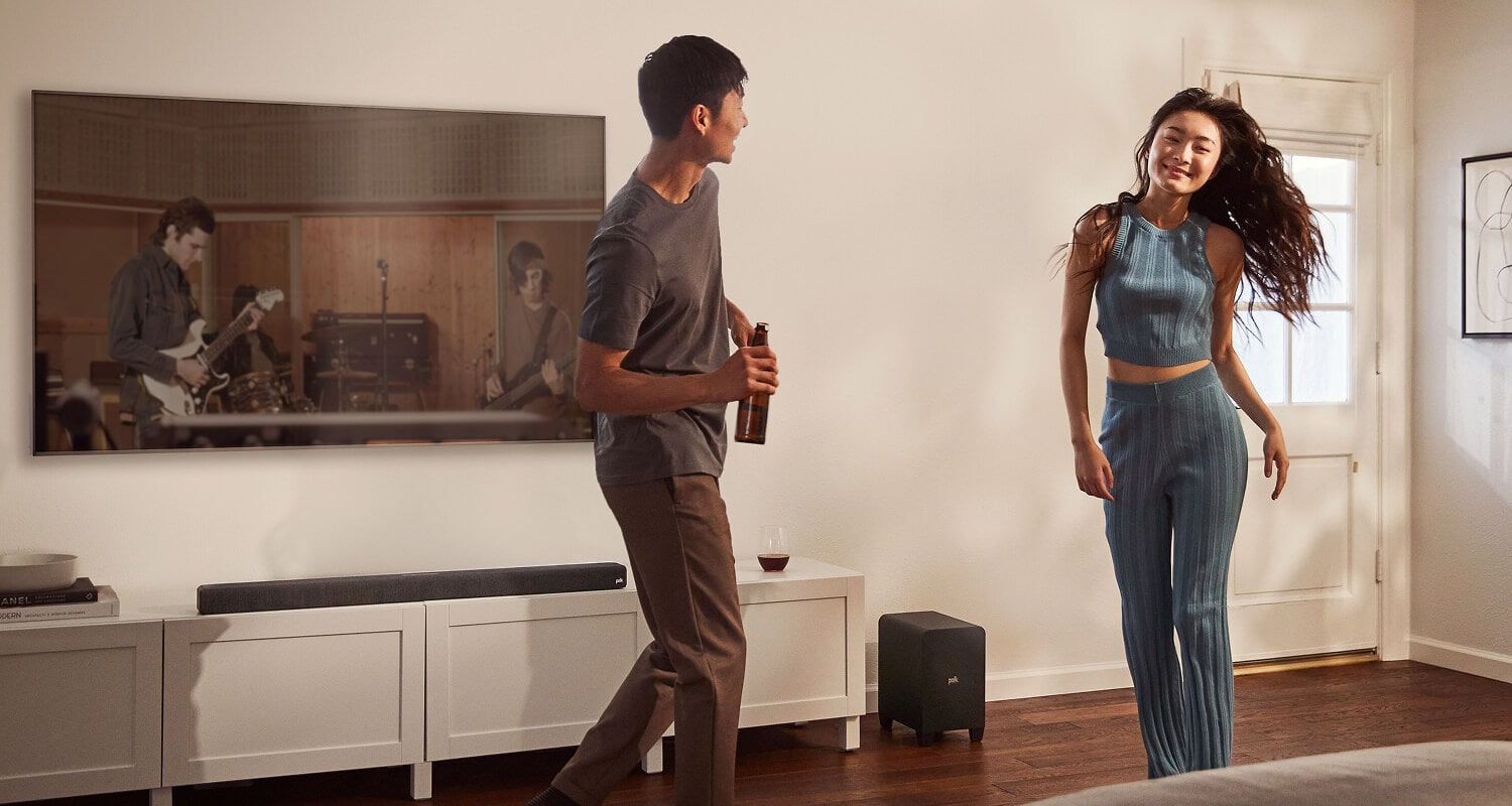 A family sitting in a room. A man controls a sound bar with a remote.